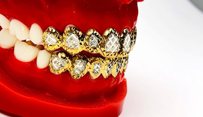 May include: A gold grill with diamond-shaped accents. The grill is made of gold and has a diamond-shaped pattern. The grill is on a red model of a mouth.