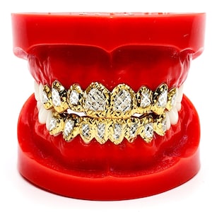 May include: A gold grill with diamond-shaped stones set in a red plastic mold. The grill is made of gold and has a diamond-shaped pattern.