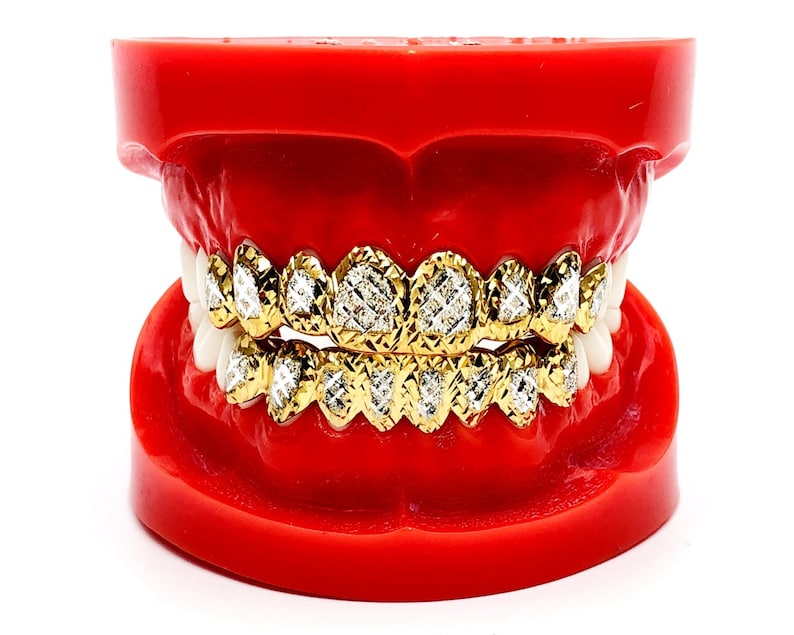 May include: A gold grill with diamond-shaped stones set in a red plastic mold. The grill is made of gold and has a diamond-shaped pattern.