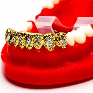 May include: Gold grill with diamond accents on a red plastic model of a mouth.