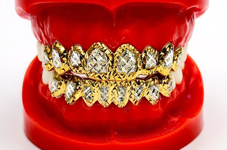 May include: Gold grill with diamond-shaped accents. The grill is displayed on a red plastic model of a mouth.