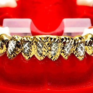 May include: Gold grill with diamond accents. The grill is made of gold and has a diamond pattern. The grill is set in a red plastic mold.