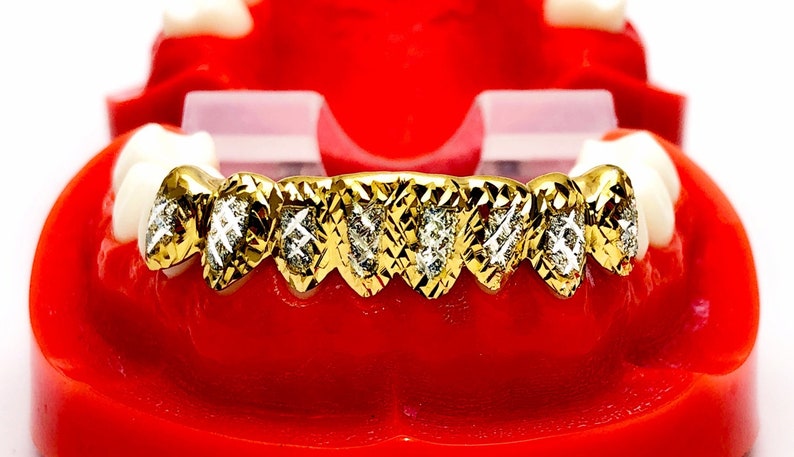 May include: Gold grill with diamond accents. The grill is made of gold and has a diamond pattern. The grill is set in a red plastic mold.