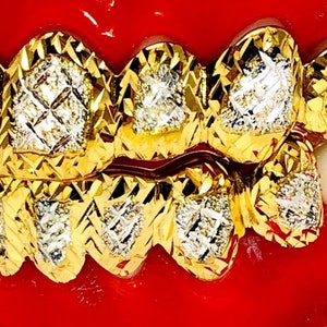 May include: A gold grill with diamond-shaped stones set in a textured gold frame. The grill is shown on a red and white model of a mouth.