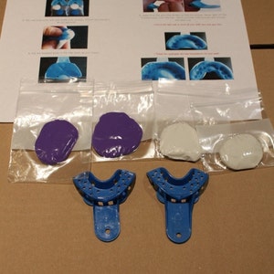 Peut inclure: Un kit de moulage dentaire avec instructions. Le kit comprend deux goutti&egrave;res bleues, deux sachets de mastic blanc et deux sachets de mastic violet. Les instructions sont imprim&eacute;es sur une feuille de papier blanche.