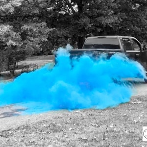 May include: A black pickup truck driving down a paved road with a blue smoke cloud trailing behind it. The smoke cloud is a gender reveal announcement.