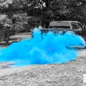 Op de afbeelding: Een zwarte pick-up truck rijdt over een geasfalteerde weg met een blauwe rookwolk die erachter hangt. De rookwolk is een gender reveal-aankondiging voor een babyjongen.