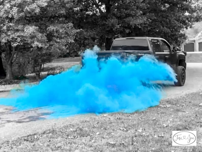 Op de afbeelding: Een zwarte pick-up truck rijdt over een geasfalteerde weg met een blauwe rookwolk die erachter hangt. De rookwolk is een gender reveal-aankondiging voor een babyjongen.