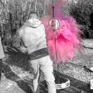 May include: A couple stands in a black and white photo, with a pink powder explosion behind them. The man is holding a black and white ball, and the woman is looking at the explosion. The text "Tori & Jon" is in the bottom right corner of the image.