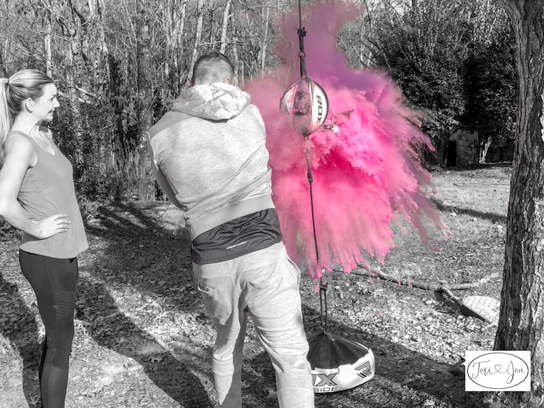 May include: A couple stands in a black and white photo, with a pink powder explosion behind them. The man is holding a black and white ball, and the woman is looking at the explosion. The text "Tori & Jon" is in the bottom right corner of the image.