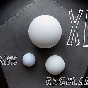 May include: Three white balls of different sizes on a gray background. The largest ball is labeled "XL", the medium ball is labeled "REGULAR", and the smallest ball is labeled "BASIC".