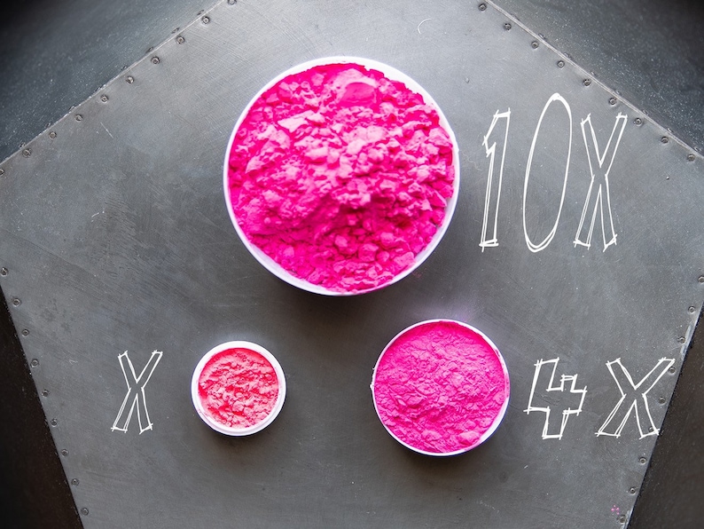 May include: Three containers of pink powder, labeled 10x, x, and 4x. The containers are on a gray metal surface.