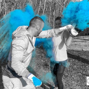 May include: Two people are facing each other in a forest setting. They are both wearing white shirts and black pants. They are holding up their hands, and blue powder is exploding around them. The text "Josi & Jon" is in the lower right corner of the image.