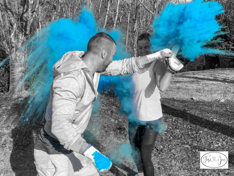 May include: Two people are facing each other in a forest setting. They are both wearing white shirts and black pants. They are holding up their hands, and blue powder is exploding around them. The text "Josi & Jon" is in the lower right corner of the image.