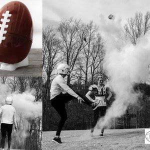 May include: A brown football-shaped container with white stripes sits on a white stand. The image shows a gender reveal with two people kicking a football, releasing a cloud of colored powder. The background features trees and a grassy field.