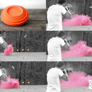 May include: A person shoots a clay pigeon with a shotgun, creating a pink cloud of smoke. The clay pigeon is orange and has a textured surface. The background is a blurred image of trees.