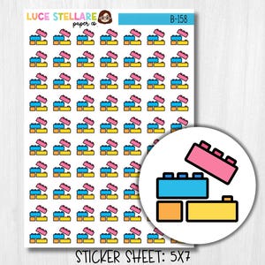 Peut inclure: Une planche d'autocollants avec des motifs de blocs de construction colorés. Les autocollants sont dans les tons de rose, bleu, jaune et orange. La feuille comprend le texte "LUCE STELLARE paper co." et "B-158". La feuille d'autocollants est étiquetée "STICKER SHEET: 5X7".