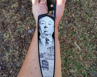 May include: A black kitchen knife with a white image of Norman Bates from the film Psycho. The image includes the Bates Motel sign and a car in the driveway.