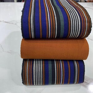 May include: A stack of three fabric strips with a striped pattern. The top and bottom strips are blue, black, white, and orange. The middle strip is solid orange.