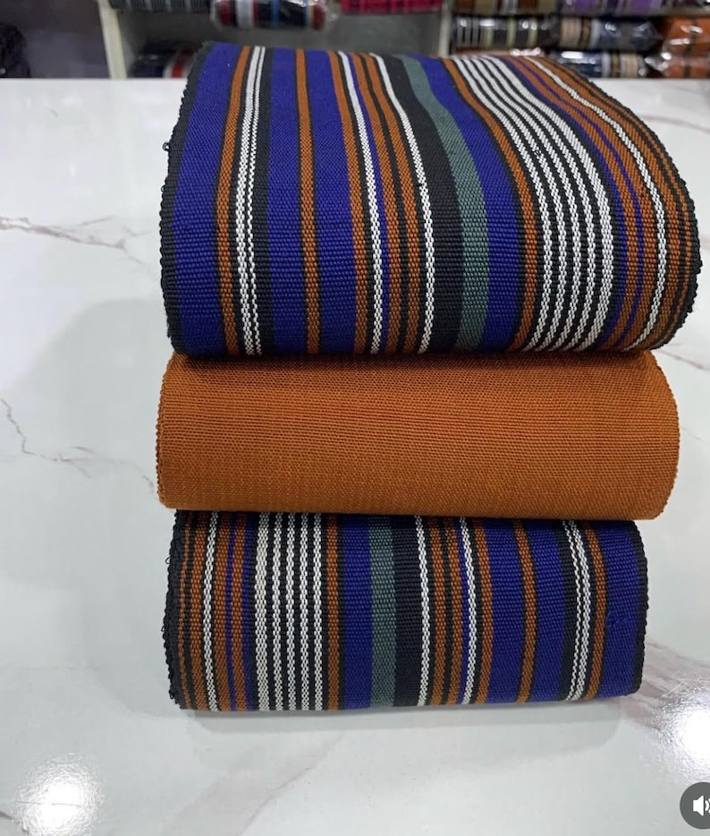 May include: A stack of three fabric strips with a striped pattern. The top and bottom strips are blue, black, white, and orange. The middle strip is solid orange.