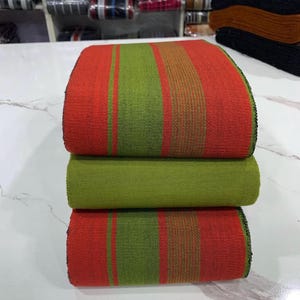 May include: A stack of three fabric strips with alternating red and green stripes. The fabric is woven and has a textured surface.