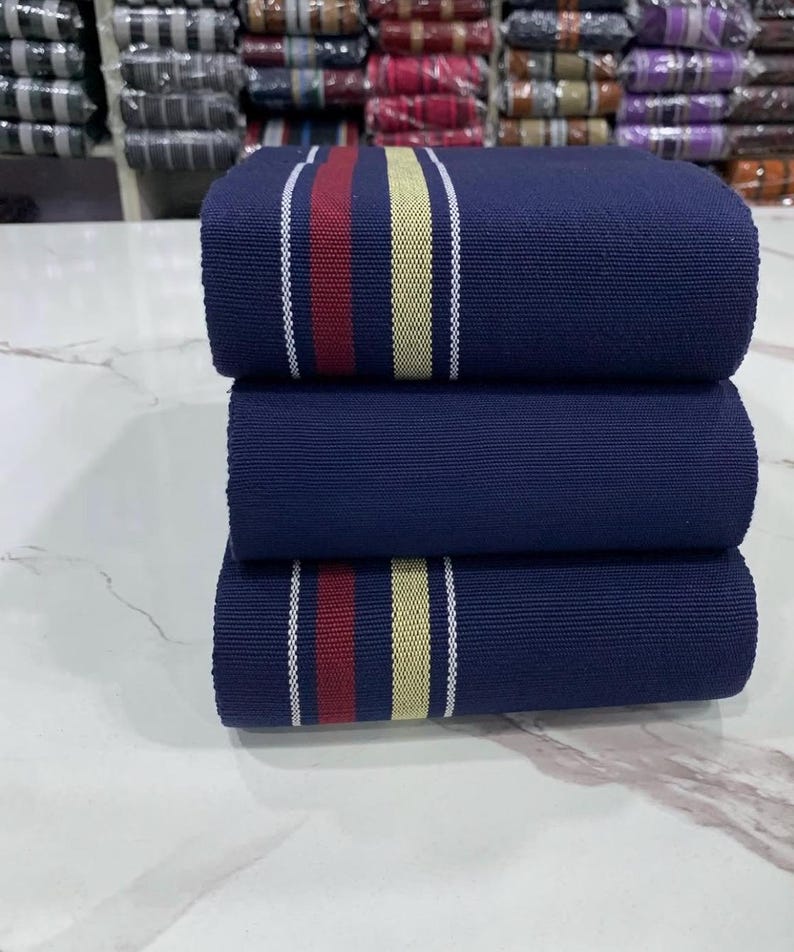 May include: Three rolls of navy blue fabric with white and cream stripes and a red stripe. The fabric is folded and stacked on a white surface.