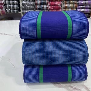 May include: Three rolls of fabric with a blue and green striped pattern. The fabric is woven with a textured surface.