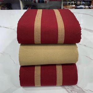 May include: Three rolls of fabric with alternating red and beige stripes. The fabric is woven and has a textured surface.
