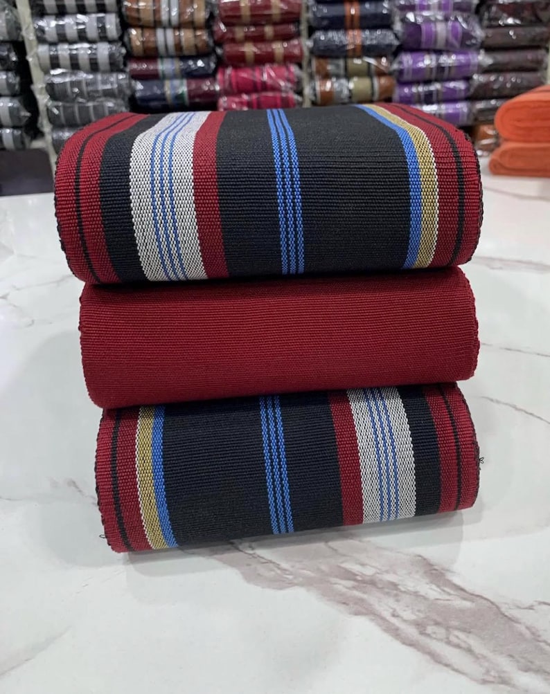 May include: A stack of three fabric rolls with striped patterns. The top roll is black with white and blue stripes, the middle roll is red, and the bottom roll is black with white, blue, and gold stripes.