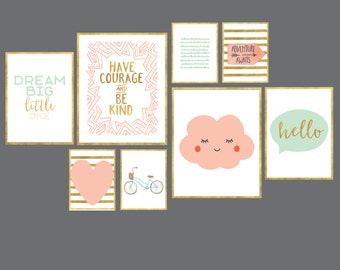 May include: A set of nine framed prints with gold frames and white backgrounds. The prints feature various illustrations and text, including a pink cloud with a smiley face, a heart, a bicycle, and text such as "Dream Big Little One", "Have Courage and Be Kind", "Adventure Awaits", and "Hello".