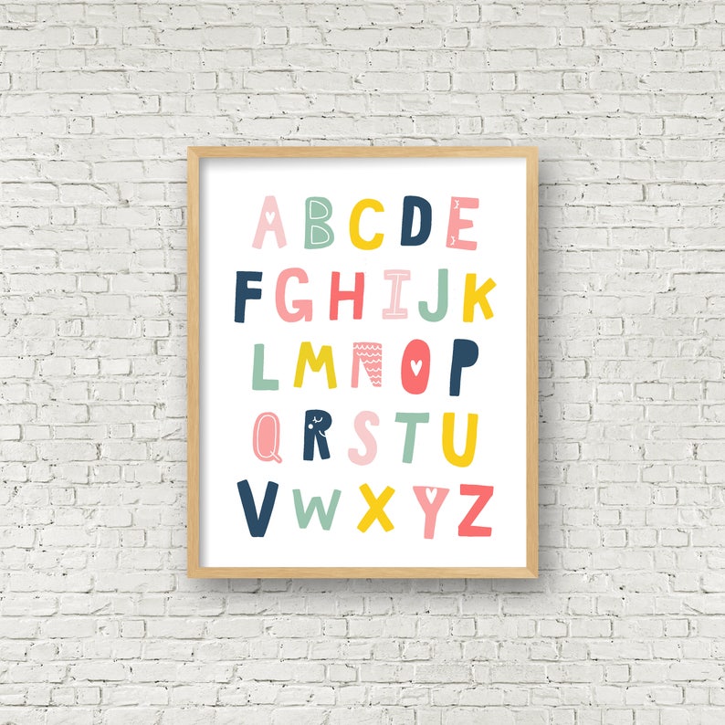May include: A framed alphabet print with colorful letters in pink, blue, yellow, and green. The letters are stylized and have different patterns and designs. The background is white.