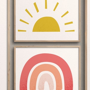 May include: Two framed prints with a minimalist design. The top print features a yellow sun with rays, while the bottom print features a pink, orange, and peach rainbow.