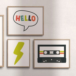 K&ouml;nnte beinhalten: Drei gerahmte Drucke an einer wei&szlig;en Wand. Der erste Druck zeigt eine Sprechblase mit dem Wort "HELLO" in bunten Buchstaben. Der zweite Druck zeigt einen gelben Blitz. Der dritte Druck zeigt ein schwarzes Kassettenband mit bunten Streifen.