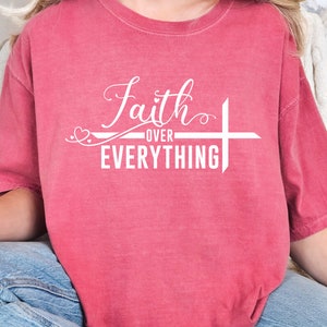 May include: A red t-shirt with a white graphic that says "Faith over Everything" with a cross and two hearts.