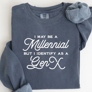 May include: A blue sweatshirt with white text that reads "I may be a Millennial but I identify as a Gen X".