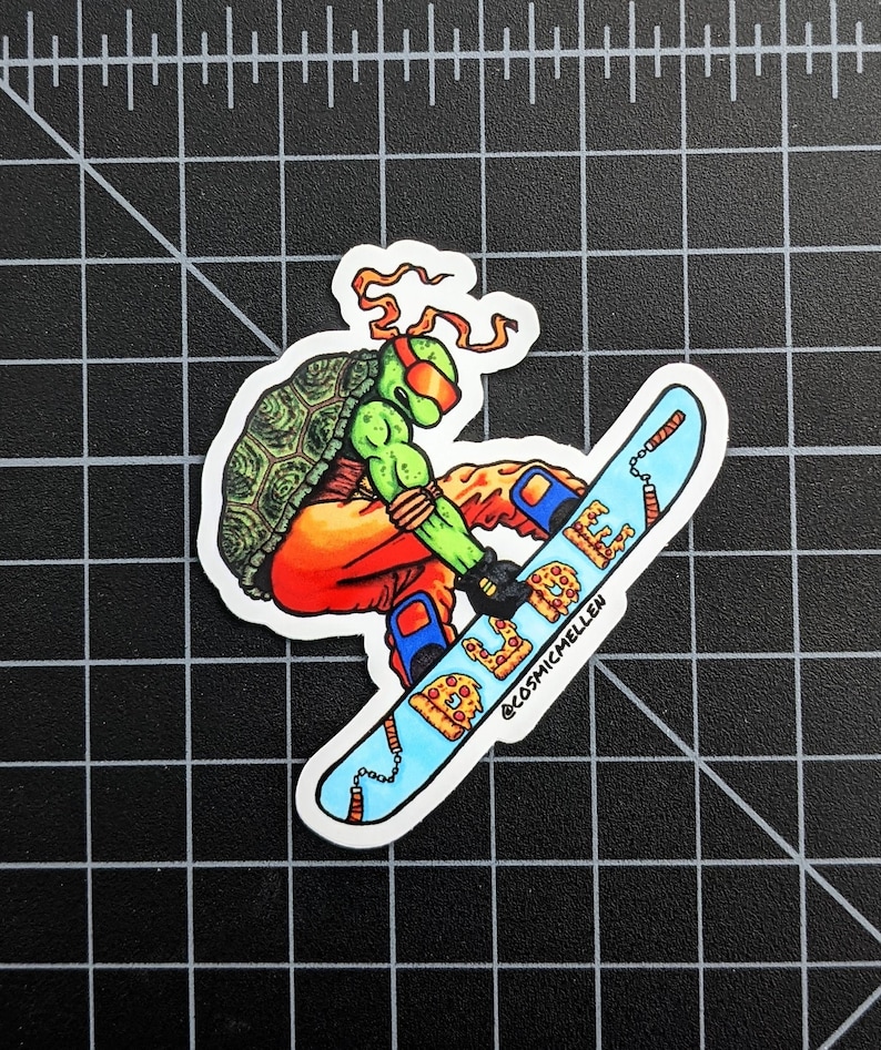 Puede incluir: Una Tortuga Ninja Adolescente Mutante verde con un pa&ntilde;uelo rojo y gafas naranjas est&aacute; haciendo snowboard en una tabla de snowboard azul y blanca con un dise&ntilde;o de pizza. La tabla de snowboard tiene una cadena y dos nunchakus rojos unidos a ella. El texto "@cosmicmellen" est&aacute; en la tabla de snowboard.
