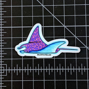 May include: A sticker of a purple and pink manta ray with a blue outline. The manta ray is swimming to the right. The sticker has the text "@cosmicmellen" at the bottom.