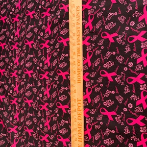 May include: Black fabric with a pink ribbon pattern. The ribbon is a symbol of breast cancer awareness. The fabric has the words "Mothers", "Sisters", "Friends", and "Daughters" printed on it.