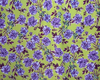 May include: A yellow fabric with a purple floral pattern. The flowers are a light purple with white accents and are arranged in a repeating pattern.