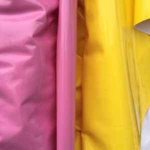 May include: Two rolls of vinyl fabric, one pink and one yellow, are folded and stacked next to each other. The fabric has a glossy finish.