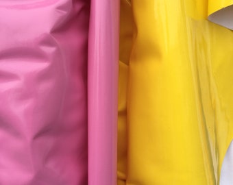 May include: Two rolls of vinyl fabric, one pink and one yellow, are folded and stacked next to each other. The fabric has a glossy finish.