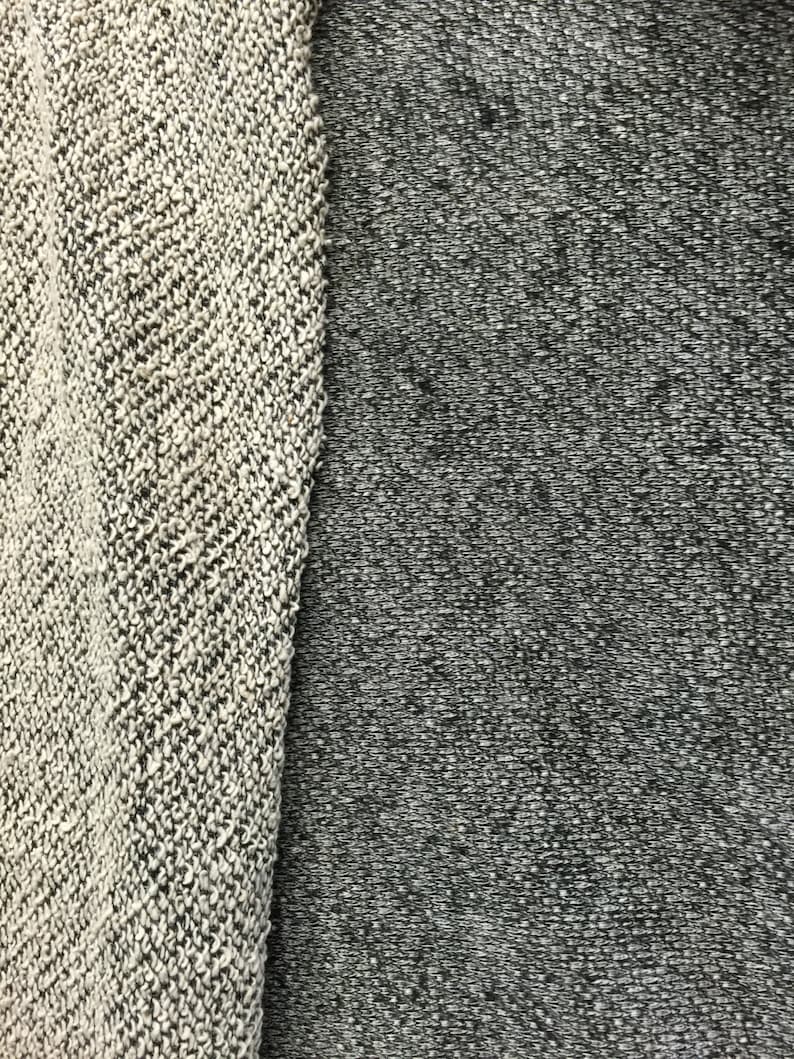 May include: Close-up of two fabric swatches. One swatch is a light gray and white knit with a textured appearance. The other is a darker gray, also with a textured appearance. The fabrics are side by side, showcasing the contrast in color and texture.