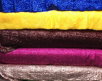 Op de afbeelding: Een stapel van paillettenstof in verschillende kleuren, waaronder rood, paars, blauw, geel, donkerrood, roze, perzik, groen, goud en zilver.