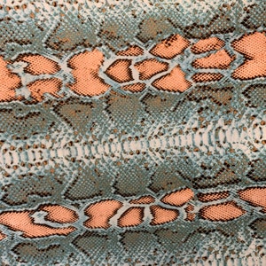 Puede incluir: Primer plano de una tela con estampado de piel de serpiente. La tela es de color azul claro con un estampado de piel de serpiente marrón y melocotón.