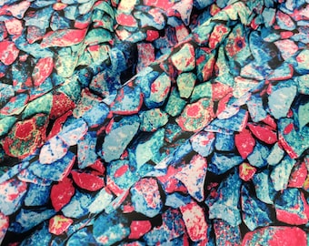 May include: Close-up of a fabric with a colorful, abstract pattern of blue, pink, and green stones. The fabric has a textured, slightly wrinkled surface.