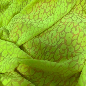 May include: Close-up of a bright green fabric with a leopard print pattern. The fabric has a subtle sheen and a slightly textured surface.