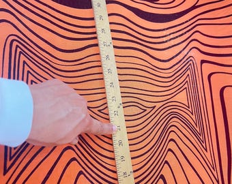 Könnte beinhalten: Orangener Stoff mit einem schwarz-weißen, wellenförmigen Muster. Ein Lineal liegt auf dem Stoff, die Zahlen 14 bis 35 sind sichtbar.