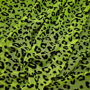 Könnte beinhalten: Grüner Netzstoff mit schwarzem Leopardenmuster. Der Stoff hat eine glitzernde Oberfläche.