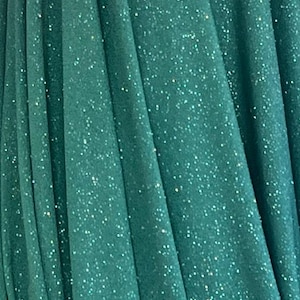 May include: Close-up of a dark teal fabric with a shimmering, glittery effect. The material is draped in soft folds, creating a textured appearance. The fabric's surface is covered in tiny, sparkling specks.