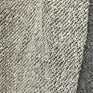 May include: Close-up of a textured fabric with a speckled pattern. The fabric is primarily off-white with black flecks, creating a heathered appearance. A section of solid gray fabric is visible on the right side, providing contrast.